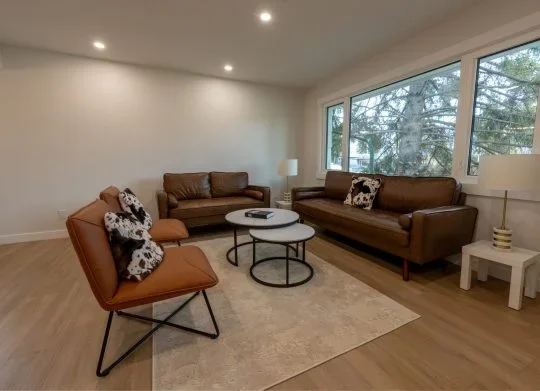 Newly remodeled living room with pot lights, brown leather furniture, and cow print throw pillows